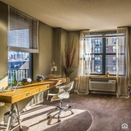 a room with a desk, chair and large windows